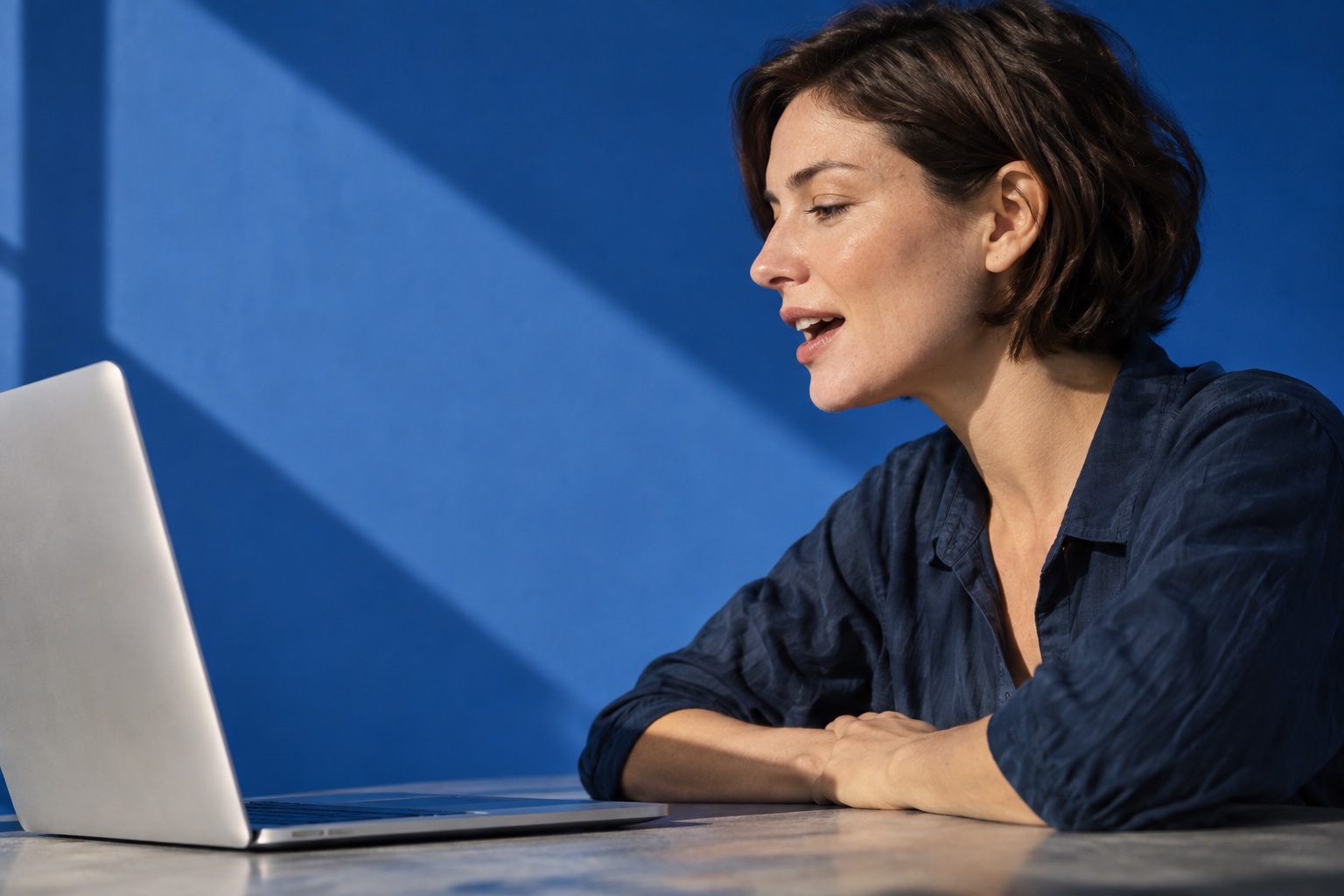 A person speaking to a laptop with their hands resting away from the keyboard.